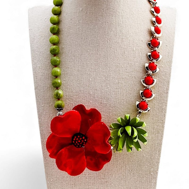 Necklace with red flower and green leaves on a beige stand against a white background