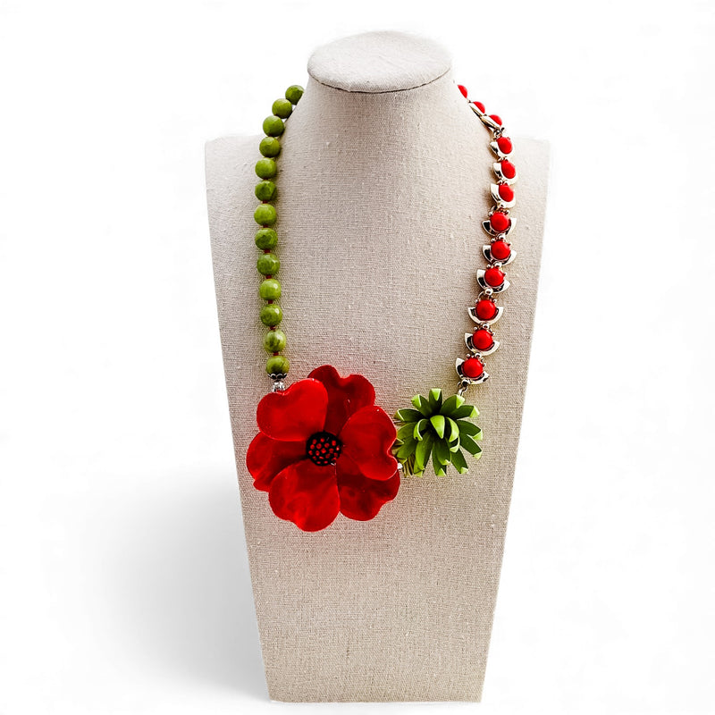 Necklace with red flower and green leaves on a beige stand against a white background