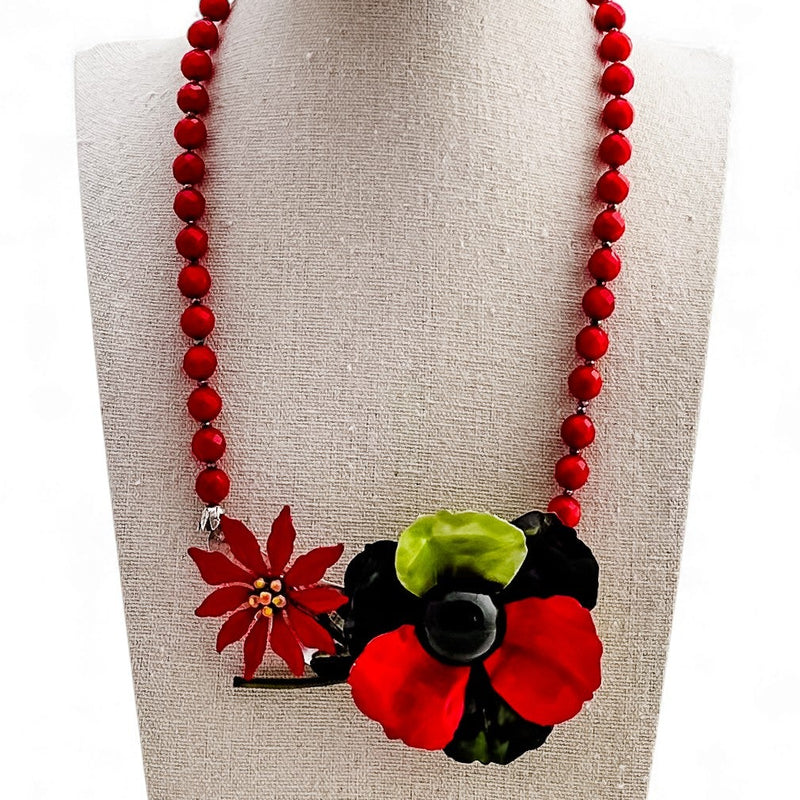 Necklace with red beads and floral pendant on a mannequin bust.