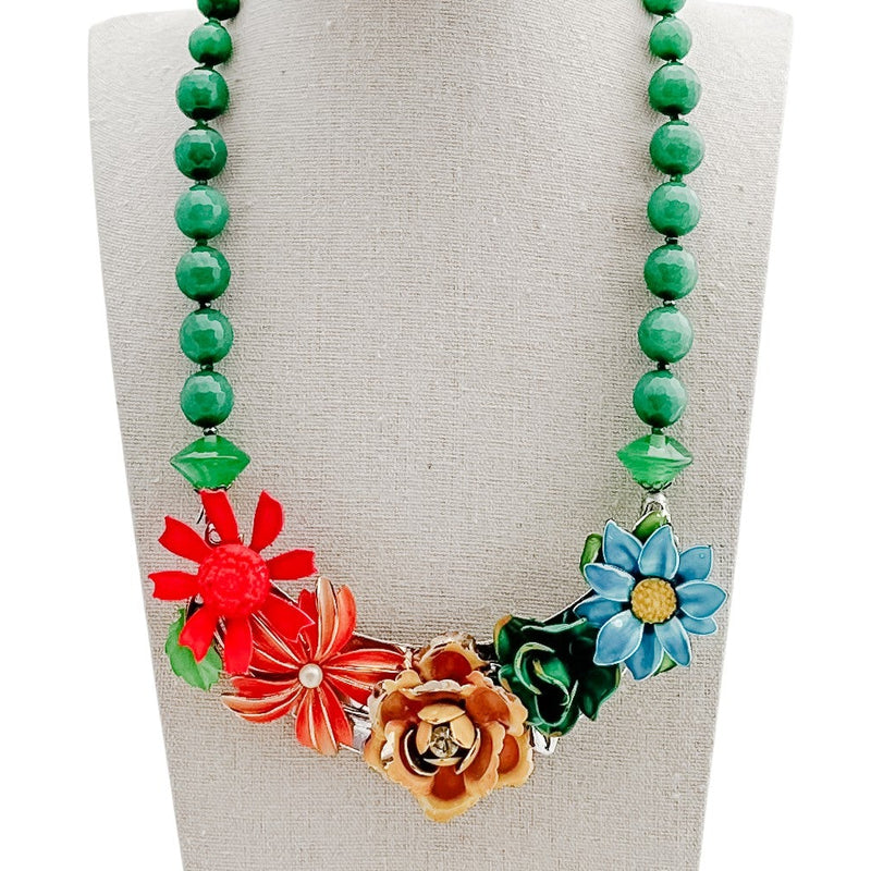 Necklace with green beads and colorful floral pendants on a mannequin bust.