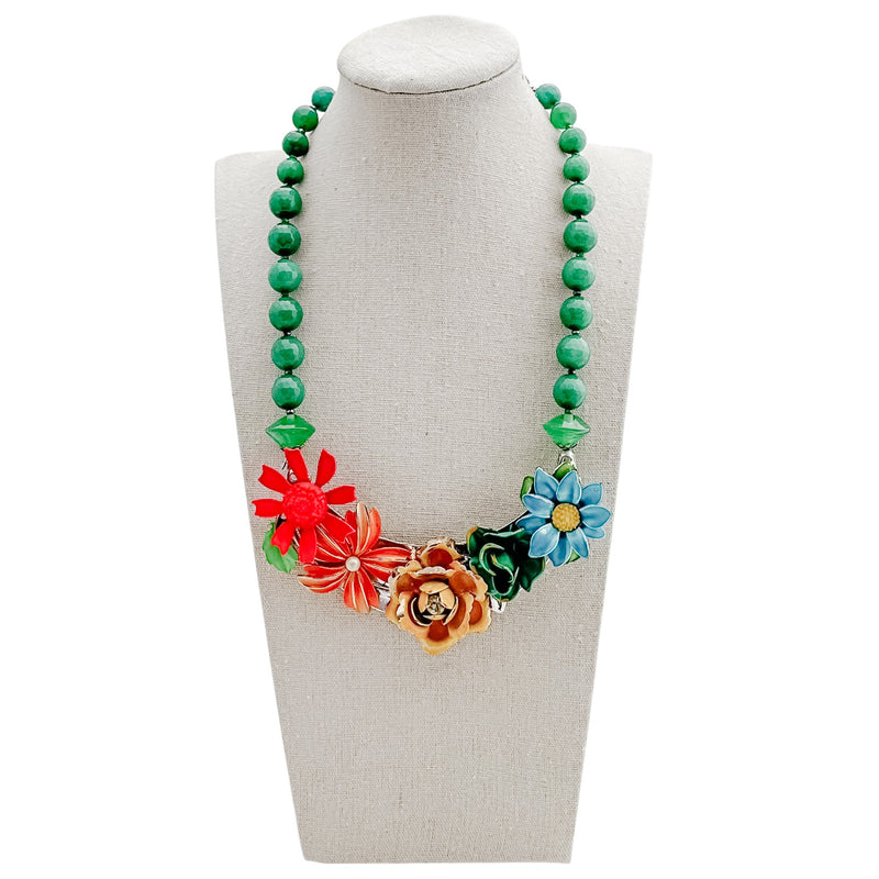 Necklace with green beads and colorful floral pendants on a mannequin bust.