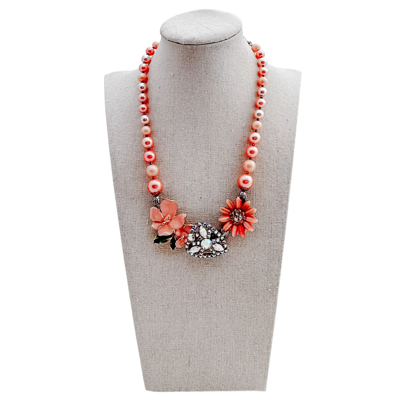 Necklace with coral beads and floral pendants on a mannequin bust.